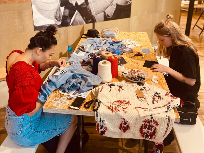 Two women are sitting at a table, mending clothes using the sashiko and boro techniques